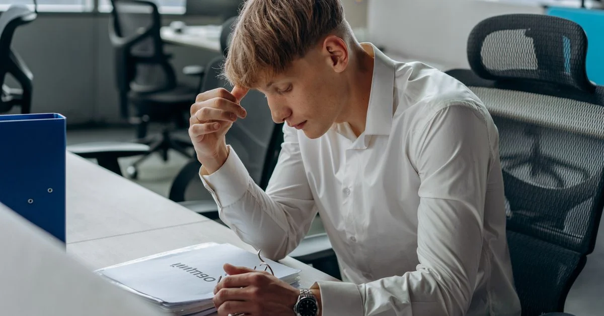 Homme en chemise blanche concentré sur la lecture de documents à un bureau moderne.