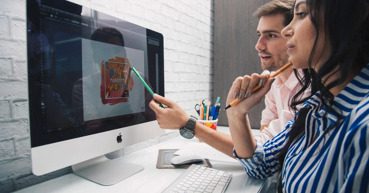 Des membres de l'équipe collaborent sur un projet de design en utilisant un ordinateur de bureau dans un bureau moderne.